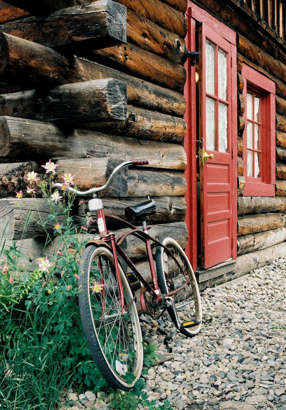 antique red cruiser bicycle leaning agains log cabin